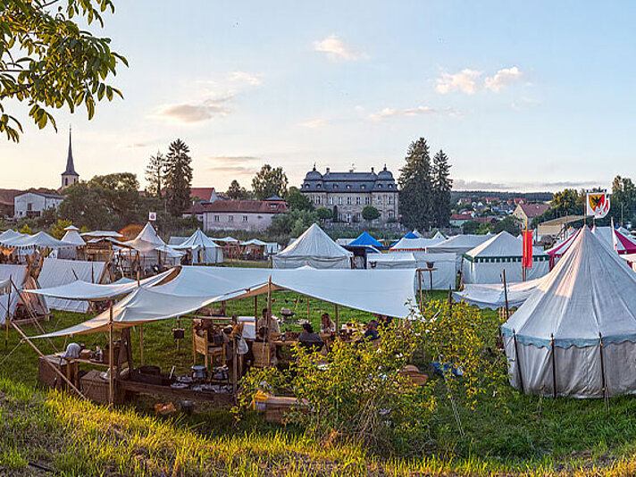 Lager mit Zelten auf einer Wiese und Barockerschloss im Hintergrund